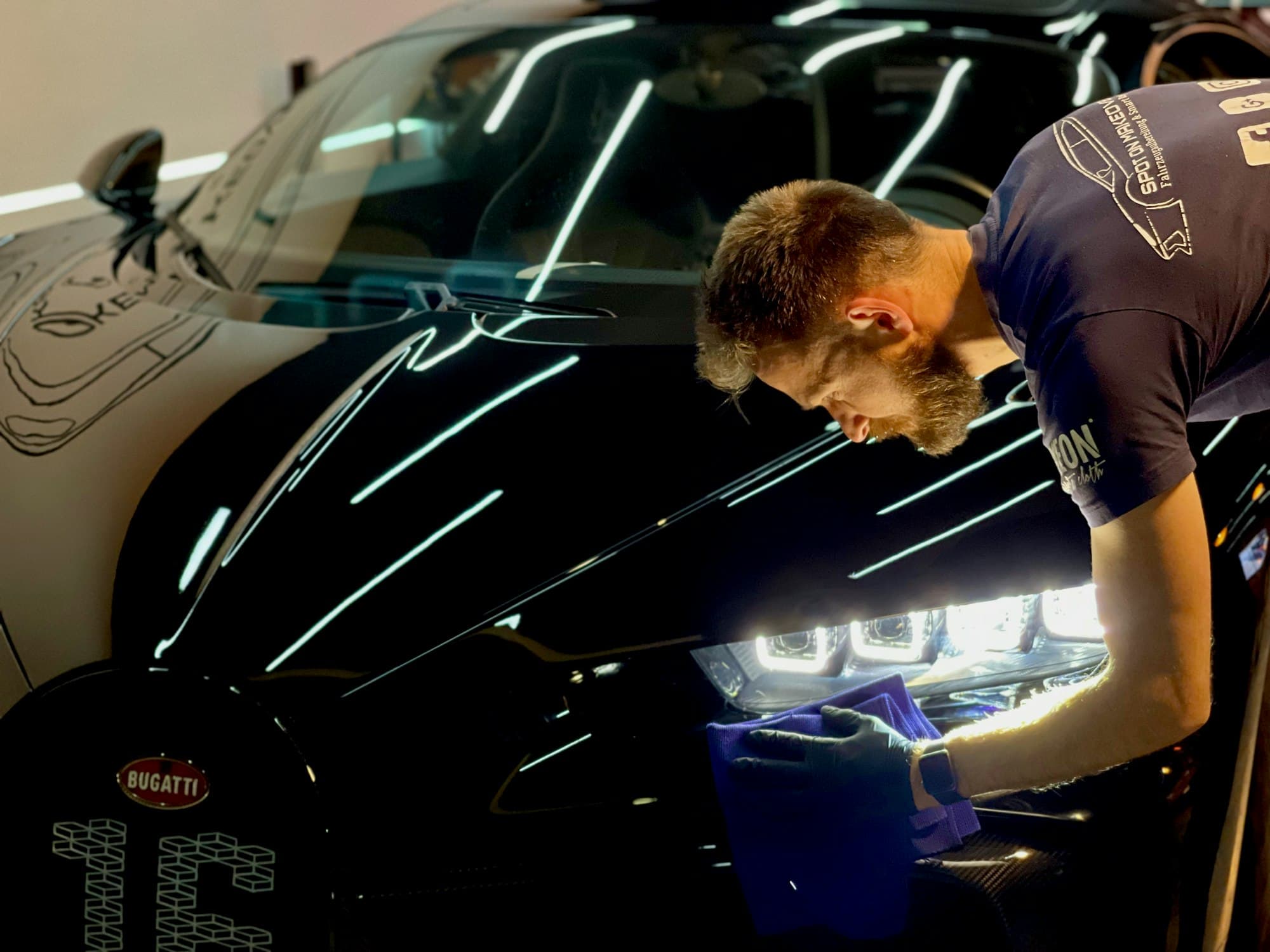 Detailer working on the hood of a black car under shop lights