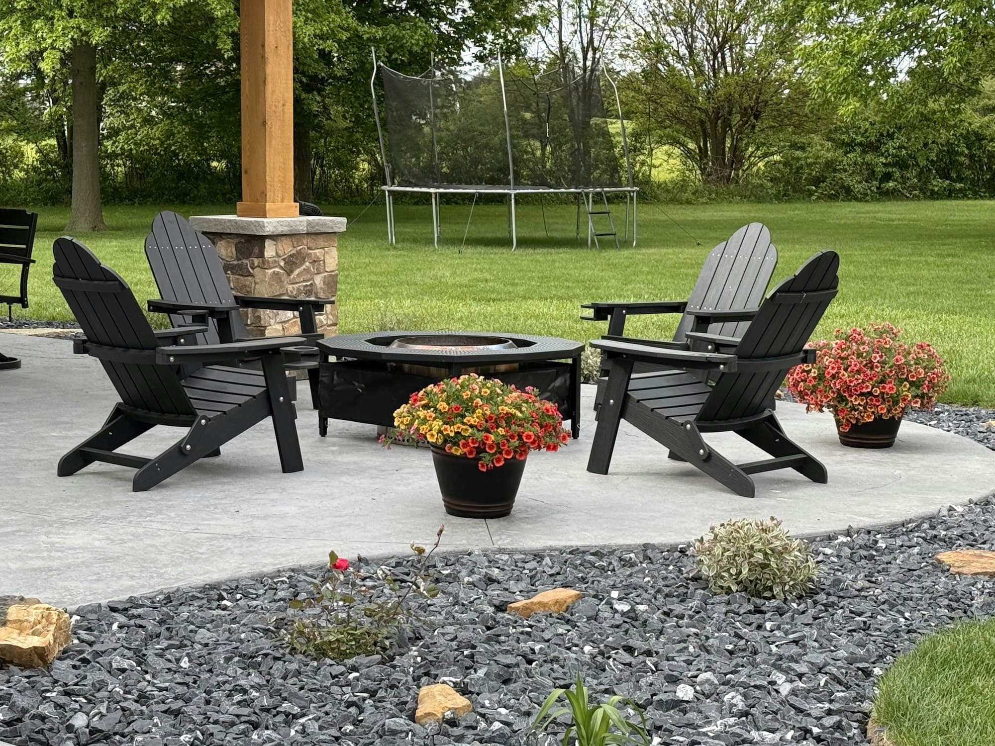 Backyard patio with Adirondack chairs around a fire pit and flower beds
